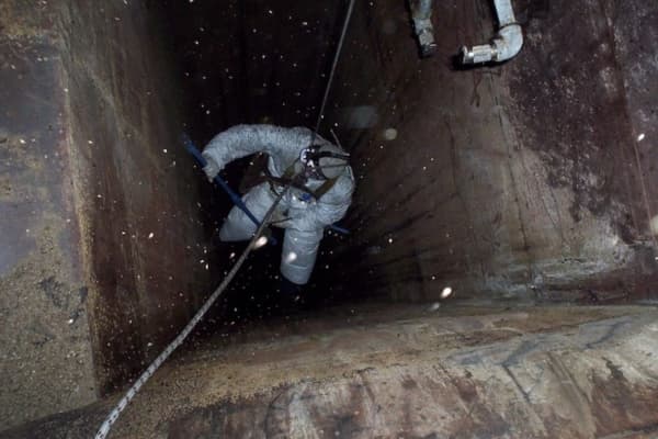 Man in a restaurant kitchen diligently cleaning the exhaust system, scraping off accumulated grease and grime.