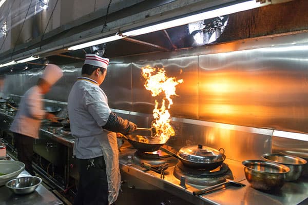 Chefs cooking with open flame beneath a commercial kitchen exhaust hood