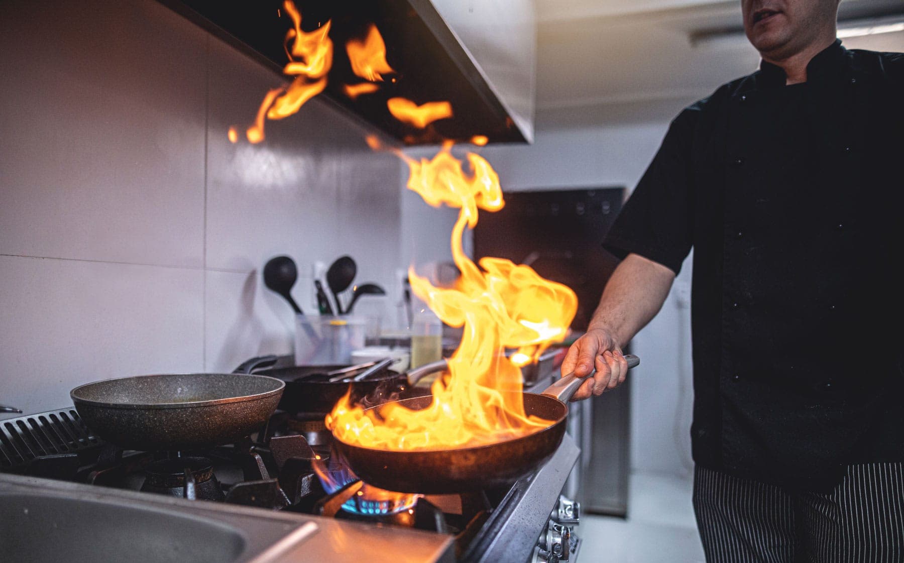 Chef flambéing beneath a commercial kitchen exhaust hood