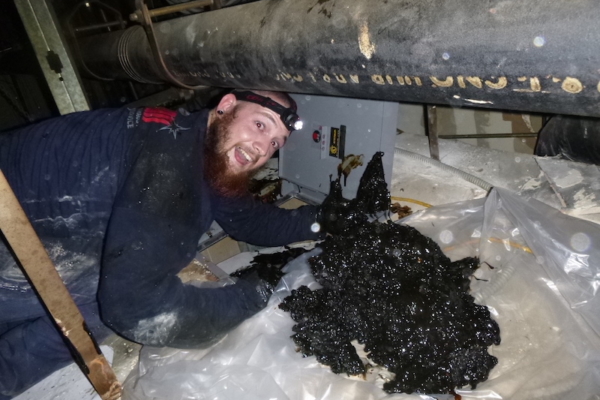 Proud hood cleaning technician displaying a thick layer of grease removed from a duct after diligent scraping, showcasing the effectiveness of their work