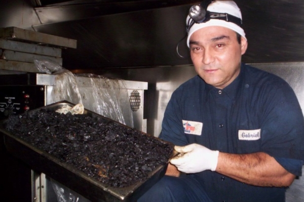 Man in a restaurant kitchen holding a handful of grease collected from the exhaust hood, showcasing the need for regular cleaning and maintenance.