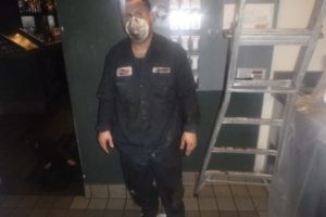 Hood cleaning technician covered in grease, standing proudly after thoroughly cleaning a kitchen exhaust system